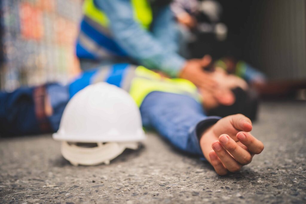 Injured construction worker lying on ground with safety helmet nearby after workplace accident.