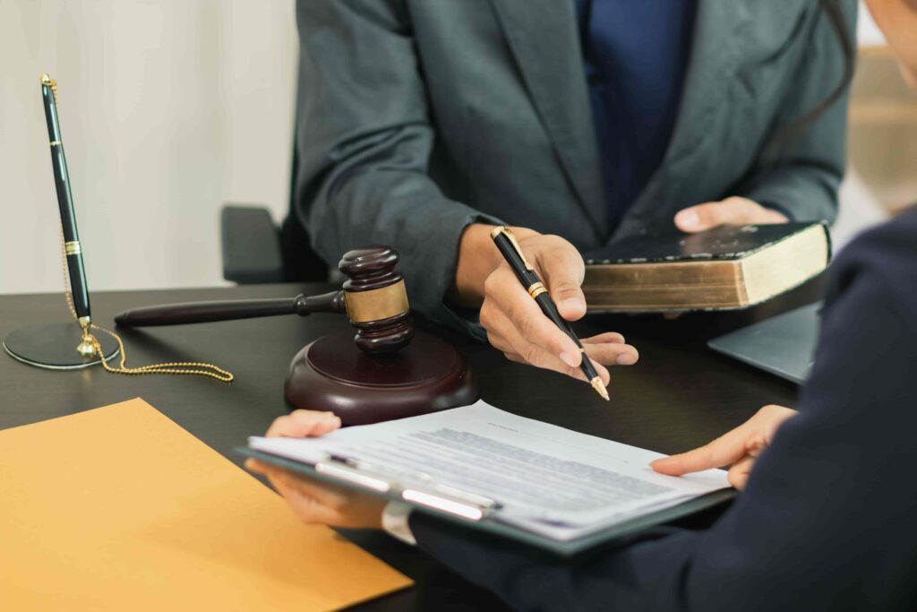 Lawyer reviewing legal documents with client in office beside gavel and law book. Lawyer reviewing legal documents with client in office beside gavel and law book.